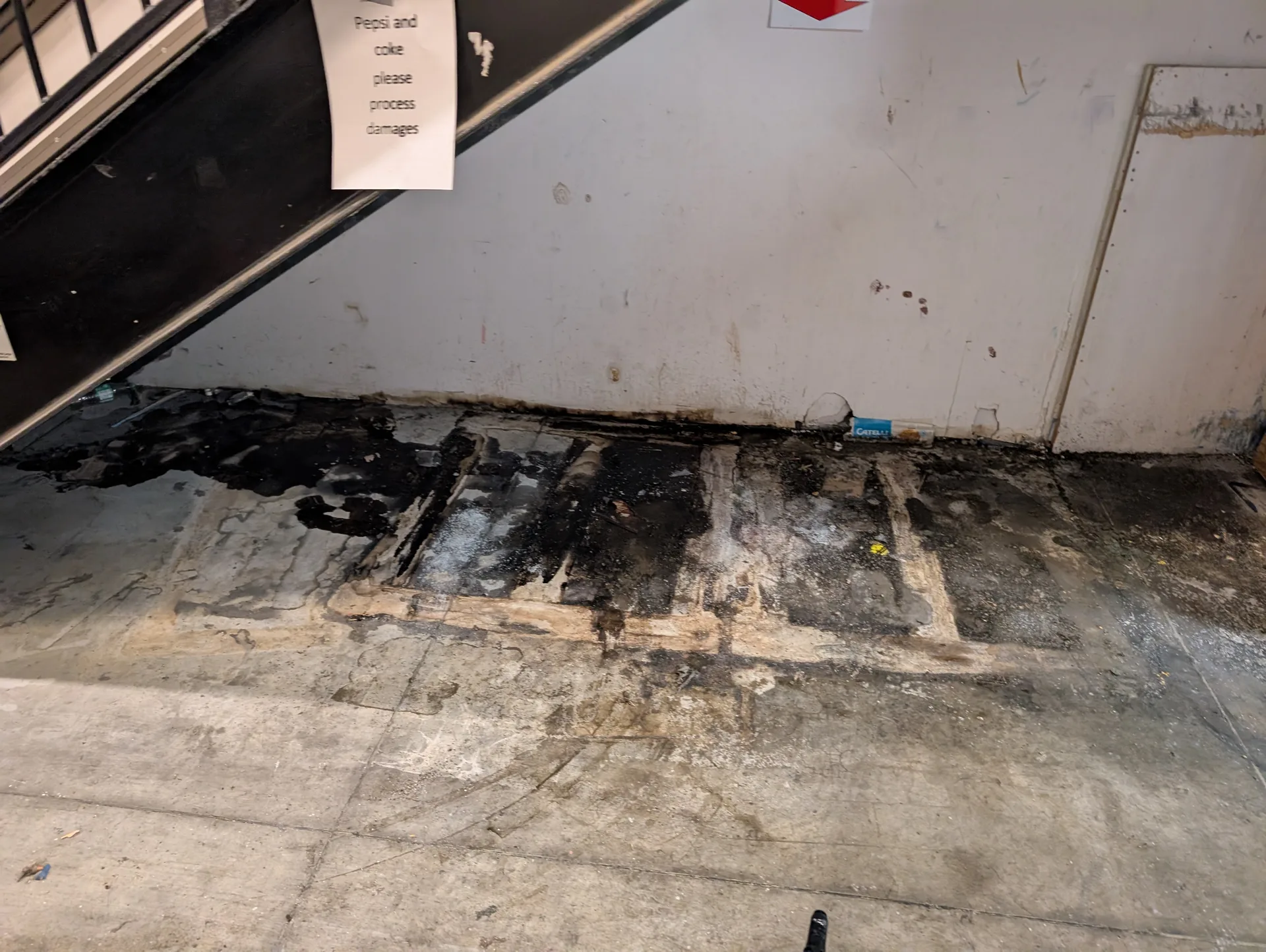 Industrial concrete floor with thick black residue under stairs before specialized deep cleaning