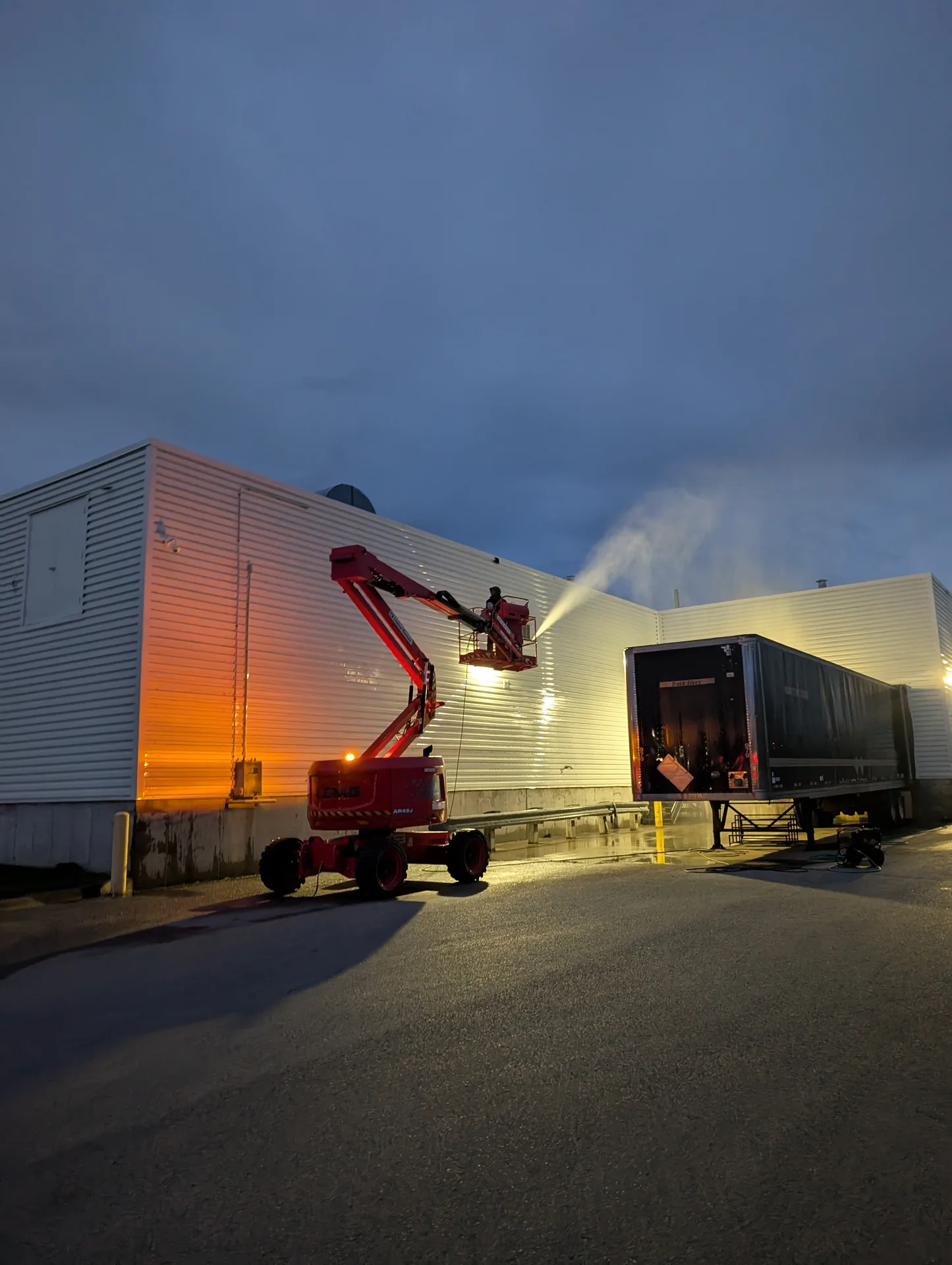 Industrial warehouse siding being soft washed by Ace Power Washing using a high-access boom lift