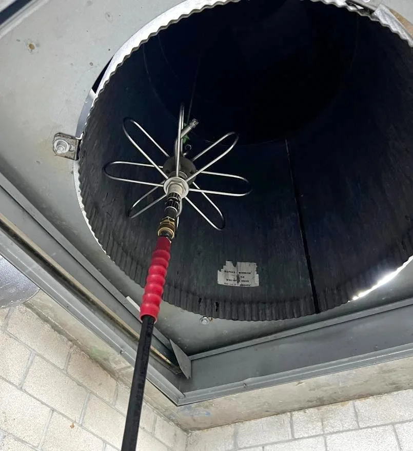 Industrial pressure washing spinner tool inside a residential rubbish chute for odor and grime removal