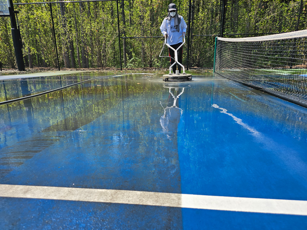 Tennis court restoration progress at midday — visible difference between cleaned and uncleaned sections